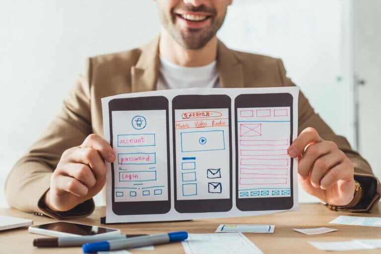 Paper wireframes of three phone screens showing a login form, a search bar, and a content layout