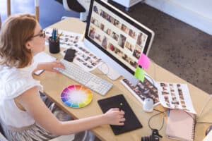 High angle view of young Caucasian female graphic designer working on graphic tablet and computer at desk in office.