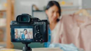 Young Asia lady fashion designer using mobile phone receiving purchase order and show clothes recording video live streaming online with camera. Small business owner, online market delivery concept.