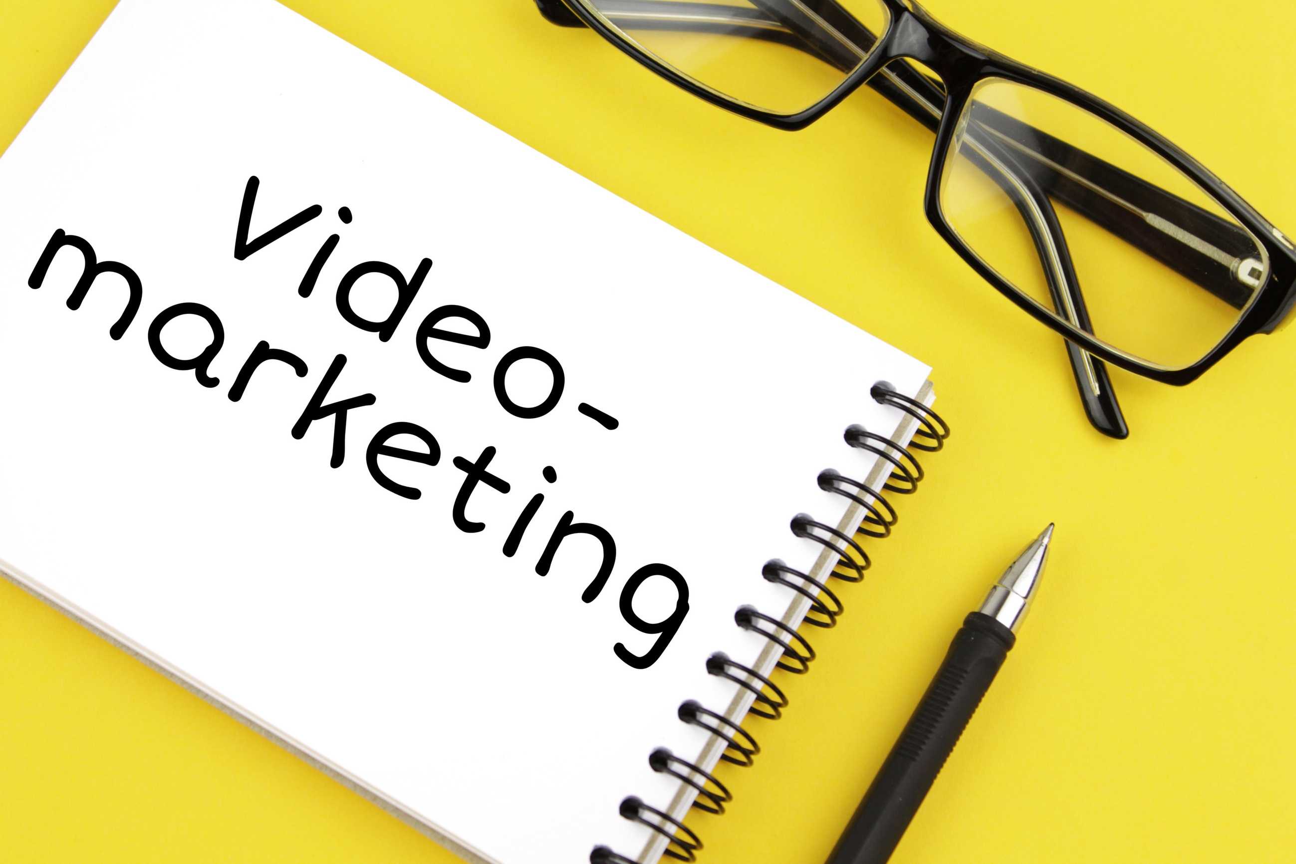 video marketing written on pad with pen and eyeglasses