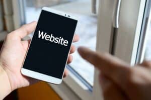 A person sees a white inscription on a black smartphone display that holds in his hand. Website