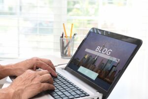 A person types on a laptop displaying a Blog Strategy Checklist on a blog webpage with a city skyline background, while a pencil holder sits nearby on the desk.