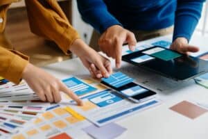 Two people review color swatches, paper mockups, and a tablet on a desk, likely discussing San Antonio Web Design options for a digital project.