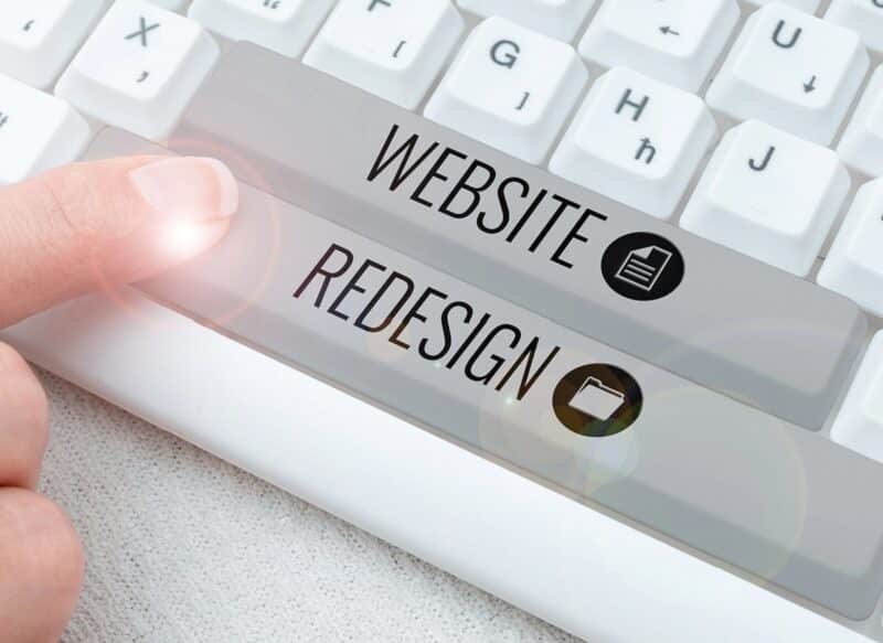 A finger presses a keyboard key labeled "WEBSITE REDESIGN" beside another key labeled "WEBSITE" on a white keyboard, representing Website Redesign San Antonio.
