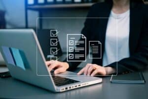 A person in business attire works on a laptop at a desk, with digital icons of checklists and documents superimposed—capturing the focus of a Website Redesign San Antonio project.