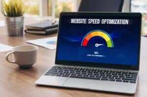 A laptop on a desk displays a Website Speed optimization screen showing a loading progress of 90%. A coffee mug, documents, and office supplies are in the background.