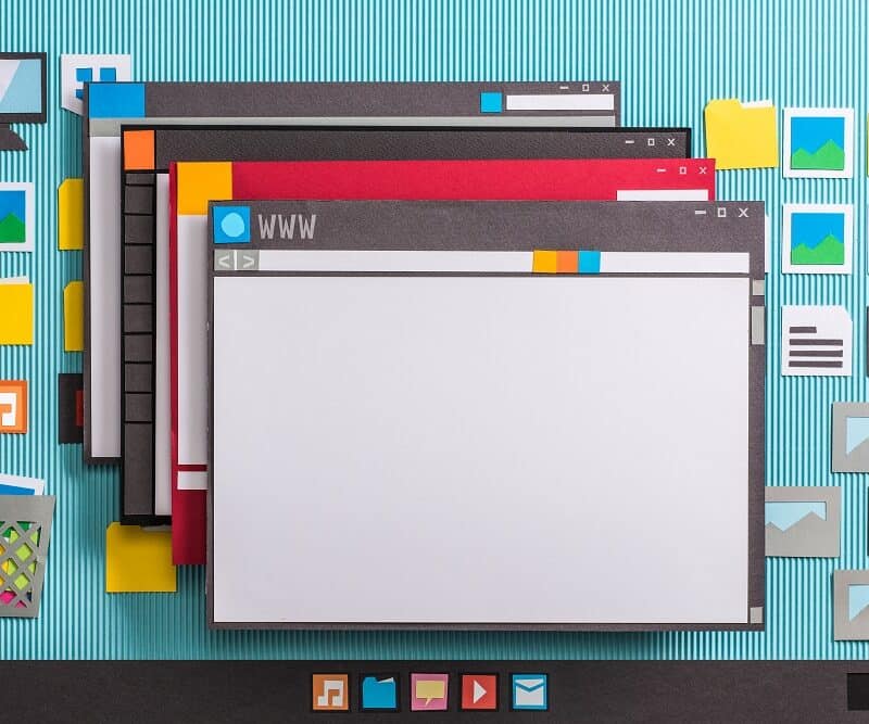Paper cutouts depict overlapping computer windows with icons for folders, images, and apps on a blue striped background, resembling a desktop interface crafted by a San Antonio Web Design Company.