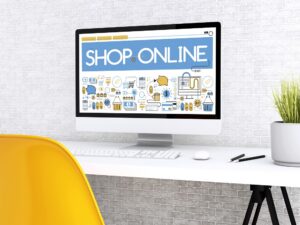 A computer monitor on a white desk displays a "Shop Online" graphic with shopping icons, hinting at Website Design Questions. A yellow chair and potted plant are next to the desk.