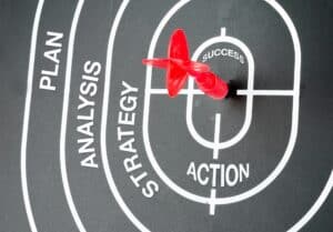 A red dart lands on the center labeled "Action" on a black target diagram with sections for "Plan," "Analysis," "Strategy," "Action," and "Success"—symbolizing steps like how to brief a web designer San Antonio professionals.