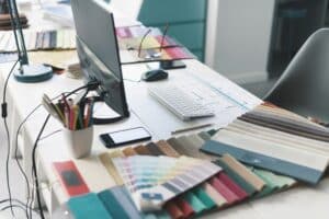 A desk with a computer, keyboard, phone, pens, and various fabric swatches and color samples spread out—perfect for brainstorming design ideas or planning how to brief a web designer San Antonio for your next project.