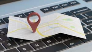 A paper map with a red location pin is placed on a computer keyboard, symbolizing navigation or online location services.