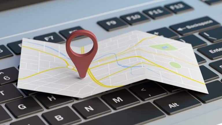 A paper map with a red location pin resting on a laptop keyboard