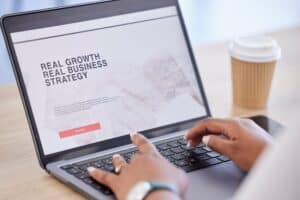 Person typing on a laptop displaying a business website with the text "Real Growth. Real Business Strategy." A disposable coffee cup sits in the background—perfect inspiration for Branding Web Design in San Antonio.
