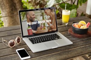 A laptop on an outdoor wooden table displays “Put your design here,” perfect for showcasing Website Design Questions. Nearby are sunglasses, a smartphone, a tropical drink, and a bowl of fruit.