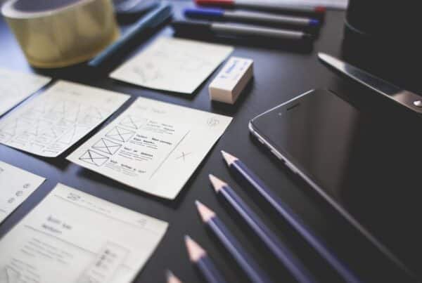 Hand-drawn website wireframe sketches, pencils, and a smartphone laid out on a dark desk during a custom web design planning session.