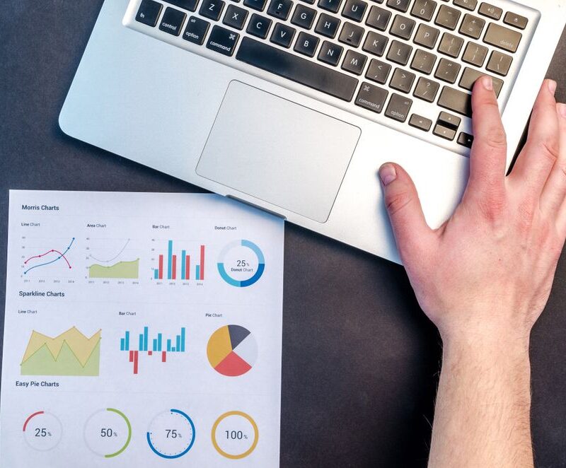 Overhead view of a printed page of colorful conversion charts and graphs next to an open laptop on a dark desk.