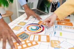 A UX design team collaborates with wireframes, interface cards, color palettes, and mobile app prototypes to improve user experience, design systems, product strategy, and digital innovation.