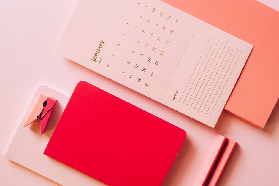 Flat lay of a monthly calendar page beside a notebook and pencils