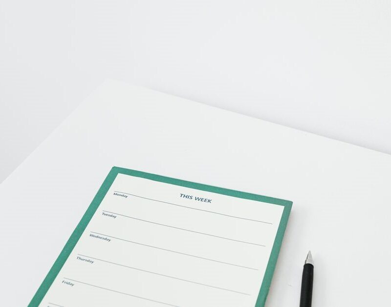 Blank weekly planner pad and a pen on a clean white desk