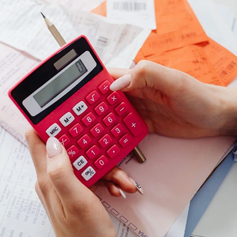 Hands using a red calculator over a pile of business receipts to weigh advertising costs