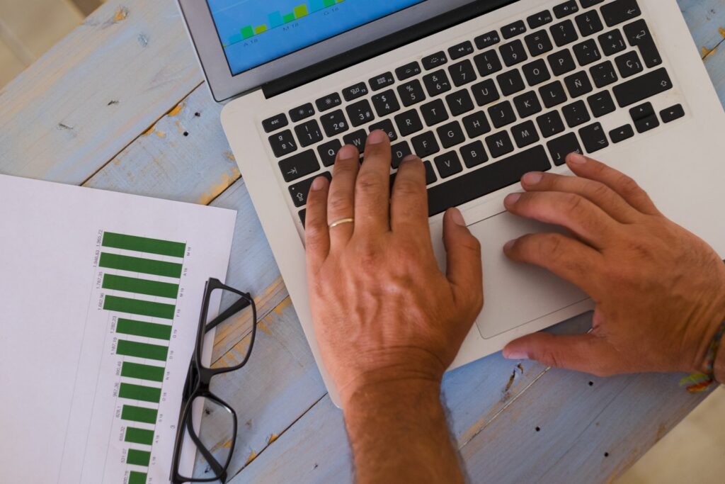 Hands typing on a laptop beside a printed bar chart and glasses