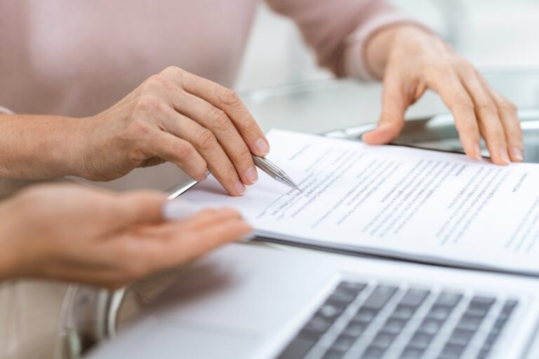 Two people review a printed agreement with a pen beside a laptop