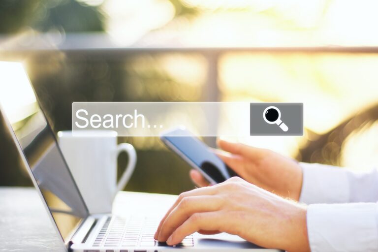 Hands typing on a laptop and holding a phone under a search bar graphic