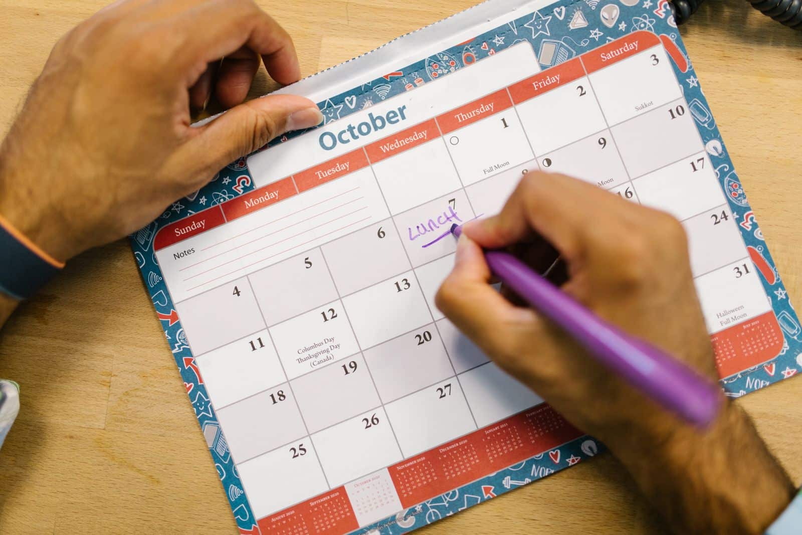 Hands marking a date on an October desk calendar